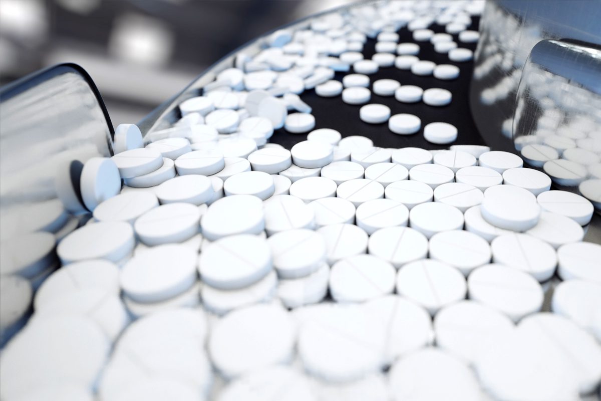 Close-up of many white round tablets moving along a conveyor belt in a pharmaceutical manufacturing facility.