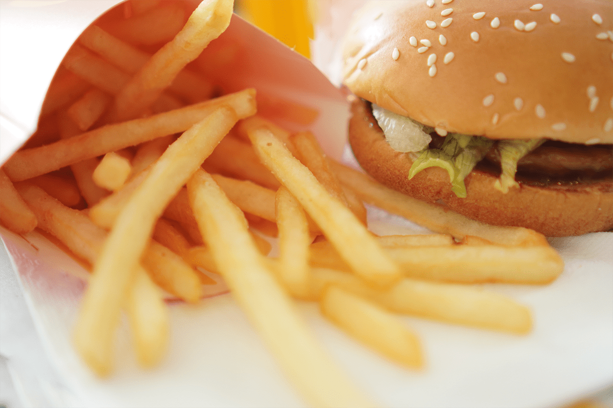 A close-up of a serving of French fries next to a sesame seed hamburger on a white surface.