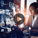 A person in business attire works on a computer displaying a digital network of profile photos, with a play button overlay indicating video content.