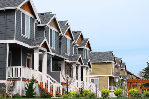 Row of modern suburban houses with gray and beige siding, white trim, porches, and neatly landscaped front yards under a clear sky.