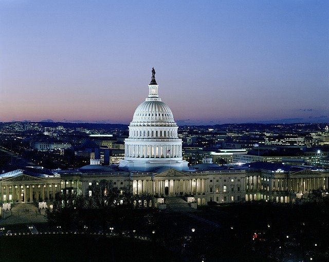 The United States Capitol building is illuminated at dusk, with city lights and a clear evening sky in the background.