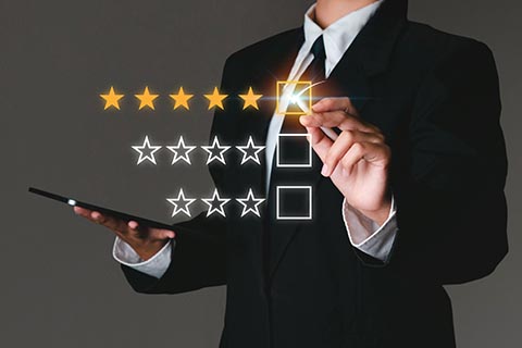 A person in a suit holds a tablet and uses a stylus to select a five-star rating on a virtual interface.