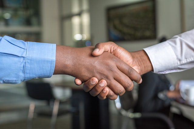 Two people wearing long-sleeve shirts are shaking hands in an office setting.