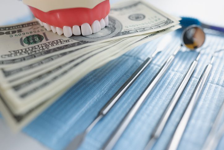 A dental model and stack of hundred-dollar bills sit next to dental tools on a blue mat.