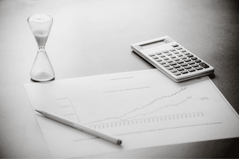 A chart with rising lines, pencil, hourglass, and calculator on a desk, suggesting financial analysis or business planning.