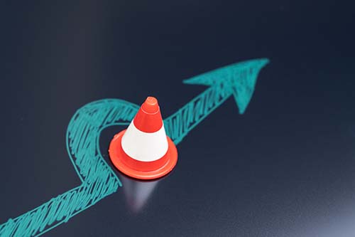 A small traffic cone sits on a drawn arrow, which curves around the cone and continues forward on a dark surface.