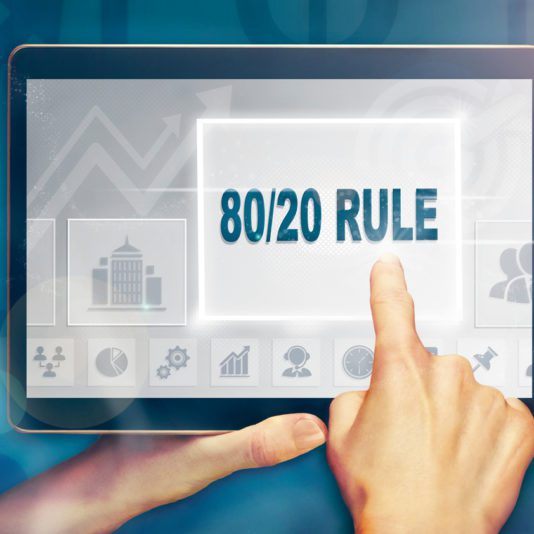 A person’s hand touches a tablet screen displaying the text “80/20 RULE” in bold letters. Various business-related icons are visible in the background.
