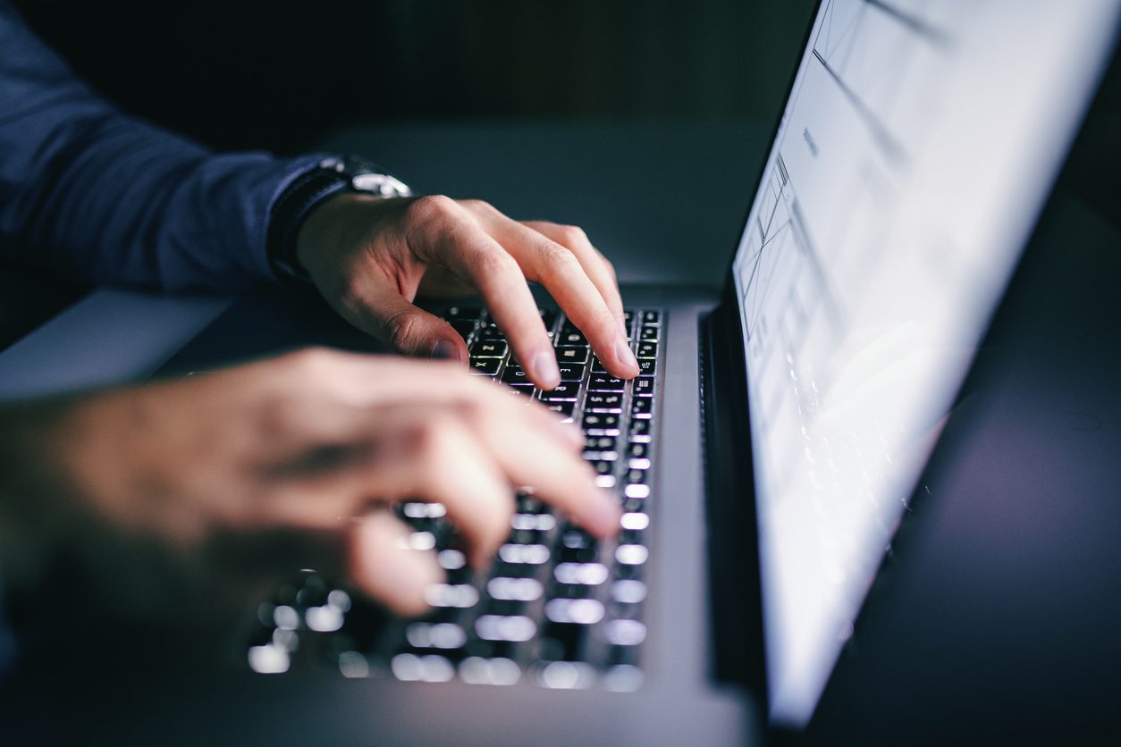 Close-up of hands typing on a laptop keyboard, with a bright computer screen in the background.