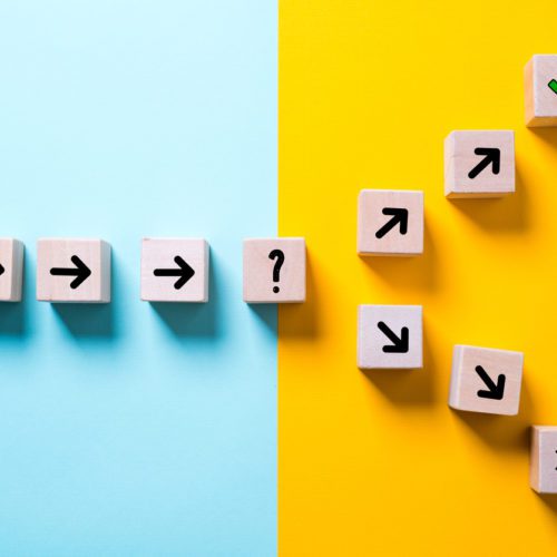 Wooden blocks with black arrows form a path on a blue background, ending with a question mark; the path splits and scatters on a yellow background.
