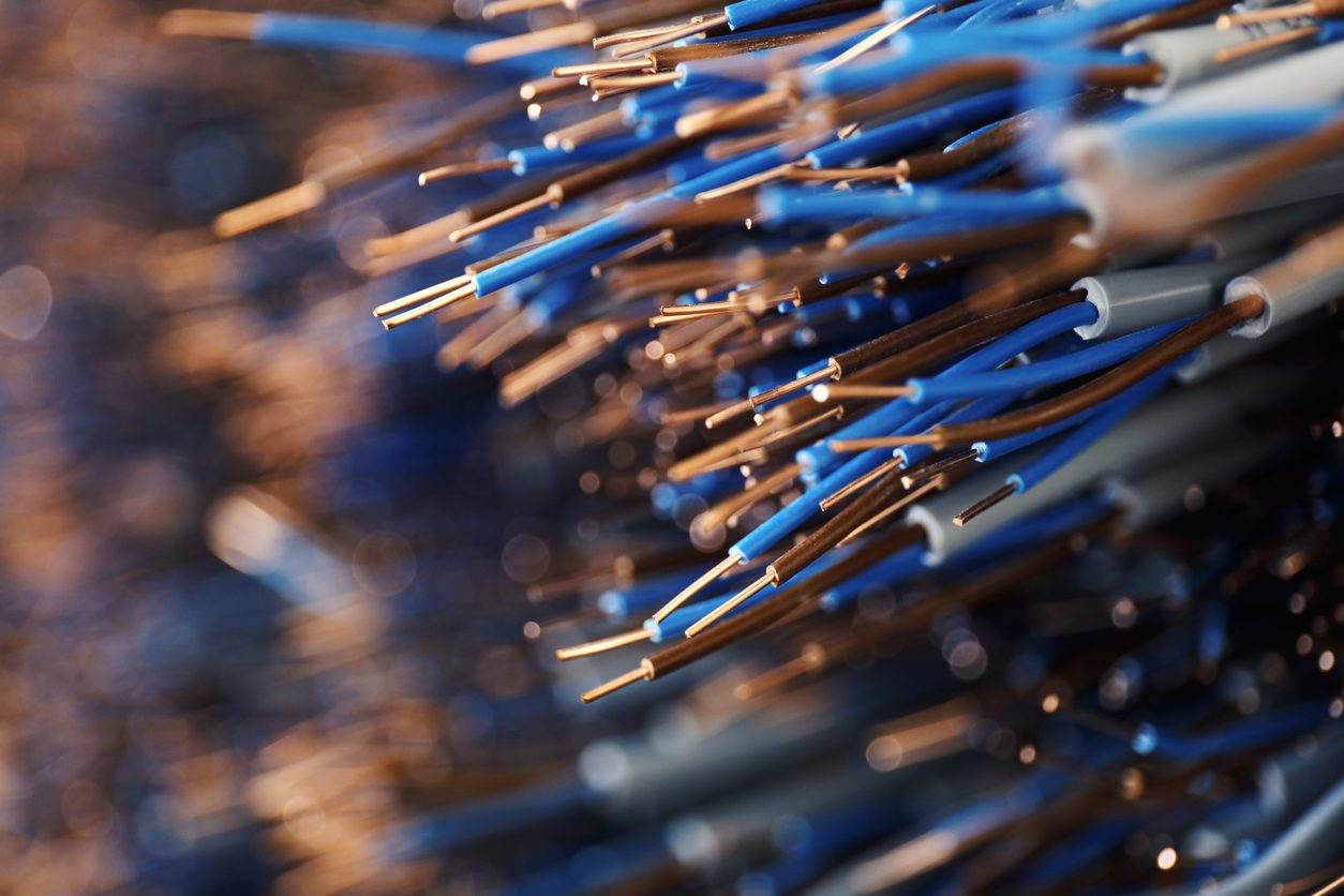 Close-up view of numerous blue and brown electrical wires with exposed copper ends, bundled together in a blurred background.