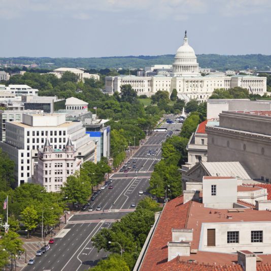 Aerial view of Pennsylvania Avenue in Washington, D.C., with the U.S. Capitol building in the background and surrounding government and office buildings.