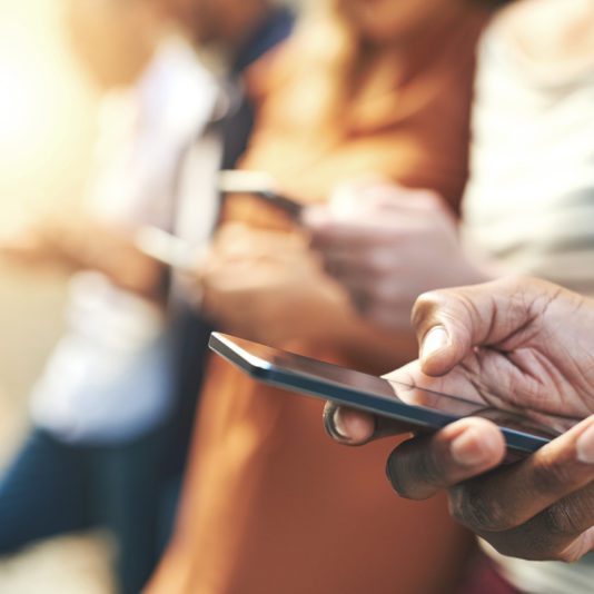 Close-up of several people standing in a row, each holding and using a smartphone, with the focus on hands and devices.