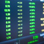 A digital screen displays rows of green stock market numbers and percentage changes, indicating positive financial performance.