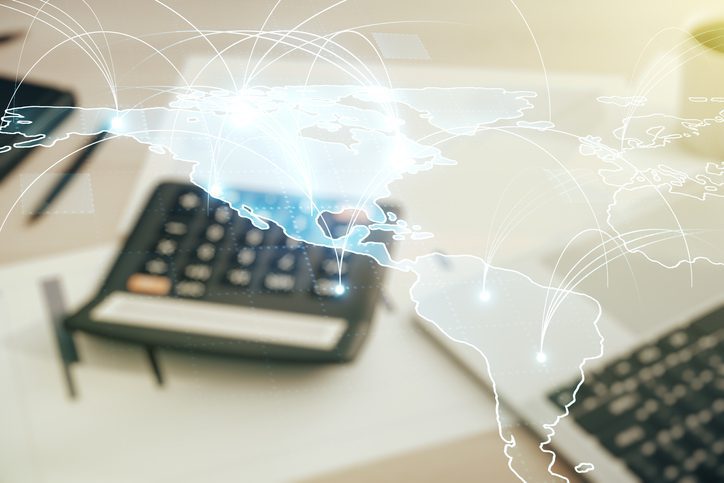 Blurred image of calculators on a desk with a digital overlay of a world map and network connections illustrating global finance or international business.