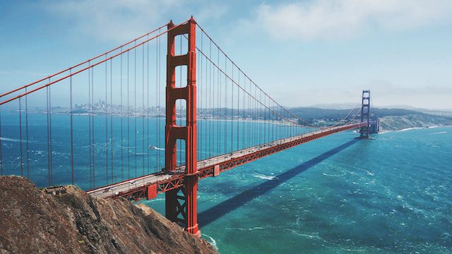 The Golden Gate Bridge spans across the blue waters of the bay, connecting San Francisco to Marin County on a clear, sunny day.