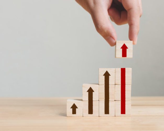 A hand stacks wooden blocks in ascending order, each block displaying an upward arrow, symbolizing growth or progress.