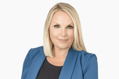 Woman with straight blonde hair wearing a blue blazer over a black top, posing against a plain white background.