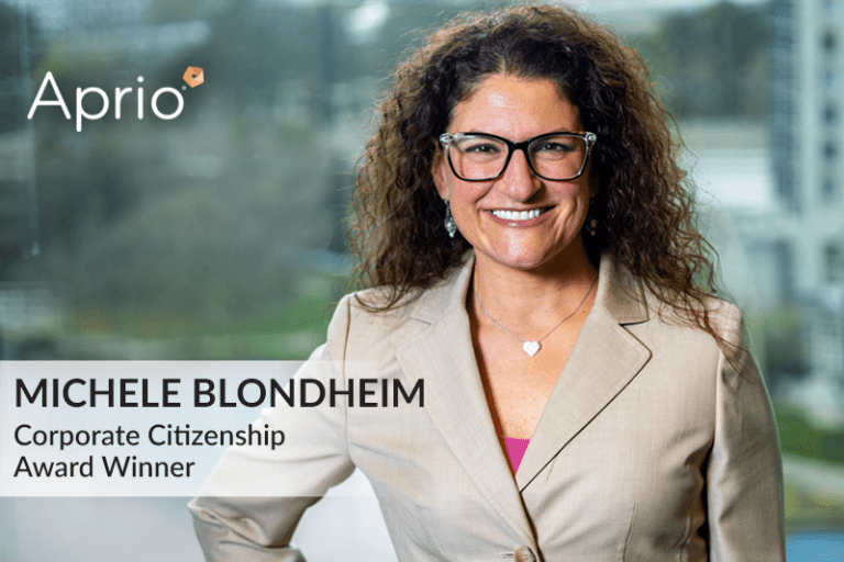 A woman in a beige blazer and glasses smiles at the camera. Text reads: Michele Blondheim, Corporate Citizenship Award Winner. Aprio logo in top left corner.