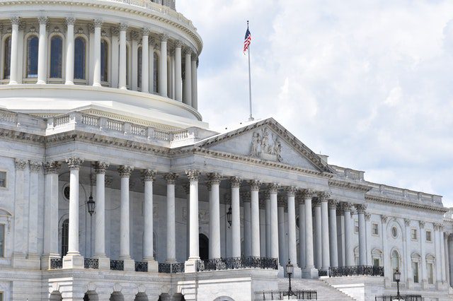 The exterior of the United States Capitol building features white columns, ornate architecture, and an American flag on a flagpole.
