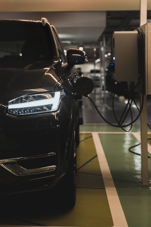 A black electric car is parked in an indoor garage, plugged into a charging station.