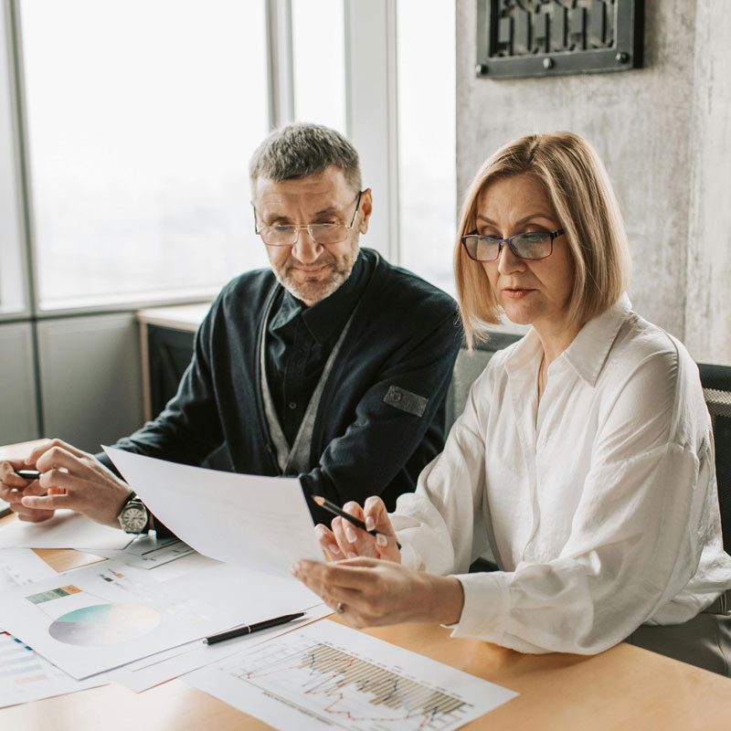 Two people sitting at a desk reviewing documents and charts in an office setting.