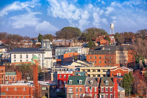 A cityscape featuring historic brick buildings, trees, and a water tower under a blue sky with scattered clouds.