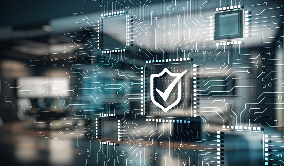 A digital illustration shows a shield with a checkmark on a computer chip, surrounded by interconnected circuit board lines, symbolizing cybersecurity in a blurred office setting.
