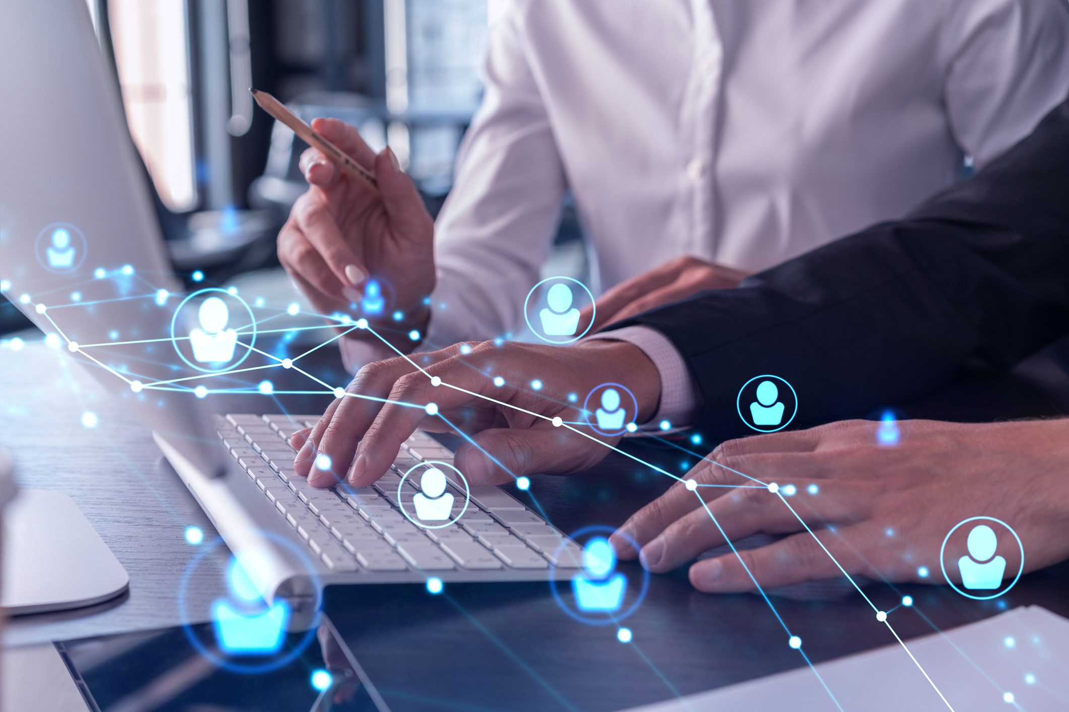 Two people work together at a computer, with digital graphics of networked user icons overlaying the image, representing online connectivity and collaboration.
