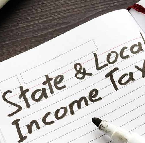 A notebook with the handwritten words State & Local Income Tax in black ink, next to an uncapped marker on a wooden surface.