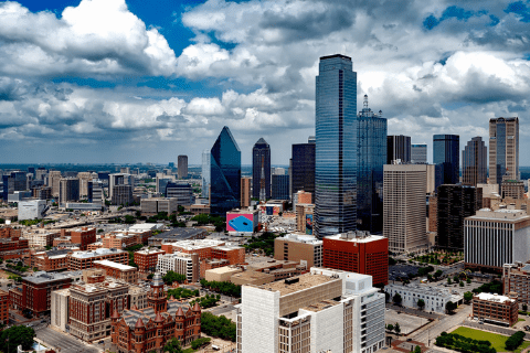 A cityscape view of downtown Dallas, Texas, featuring tall skyscrapers, mid-rise buildings, and partly cloudy skies.
