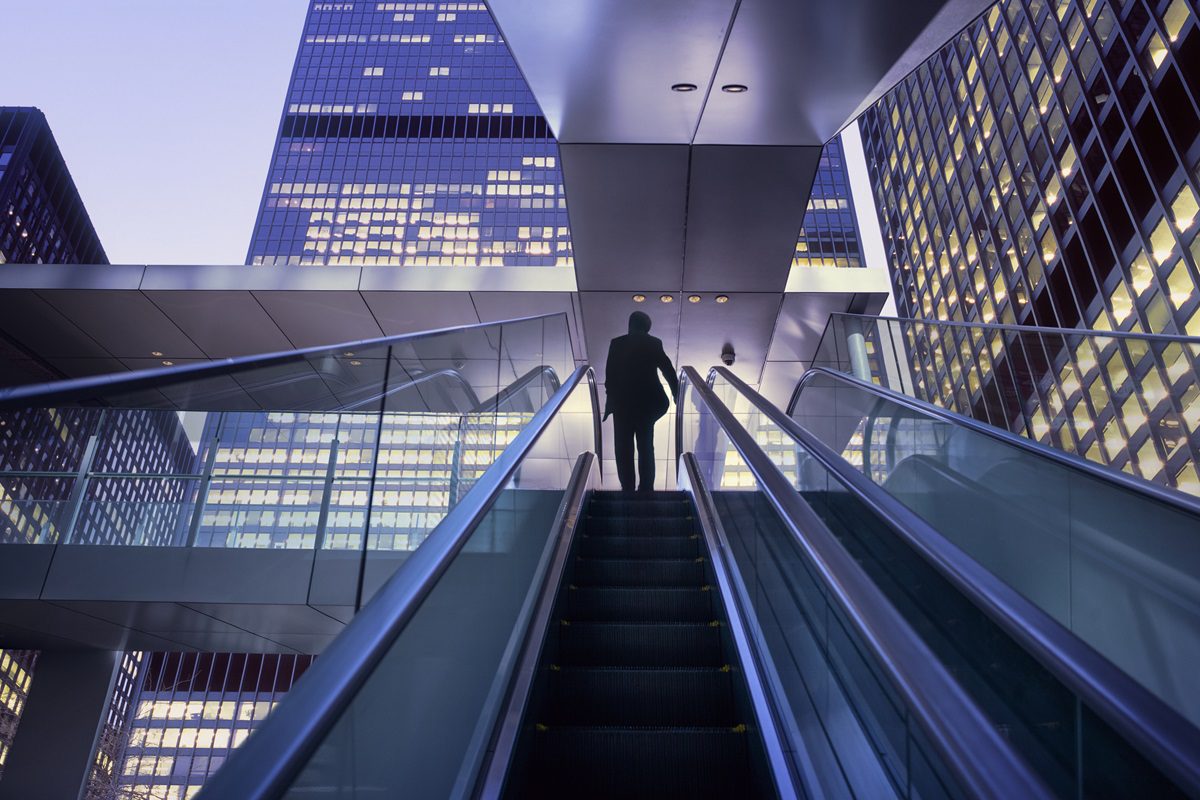 Businessman on top of moving escalator at modern illuminated business district