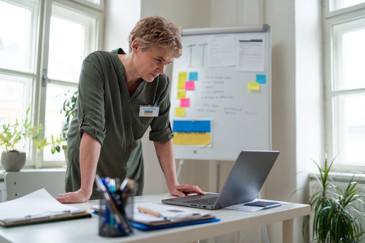 Mature woman working with laptop as volunteer for Ukrainian refugees in office.