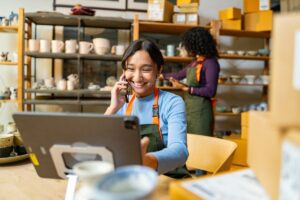 In a bustling ceramic shop, a young woman efficiently manages inventory and takes orders by phone, showcasing the seamless blend of traditional craftsmanship and modern business practices