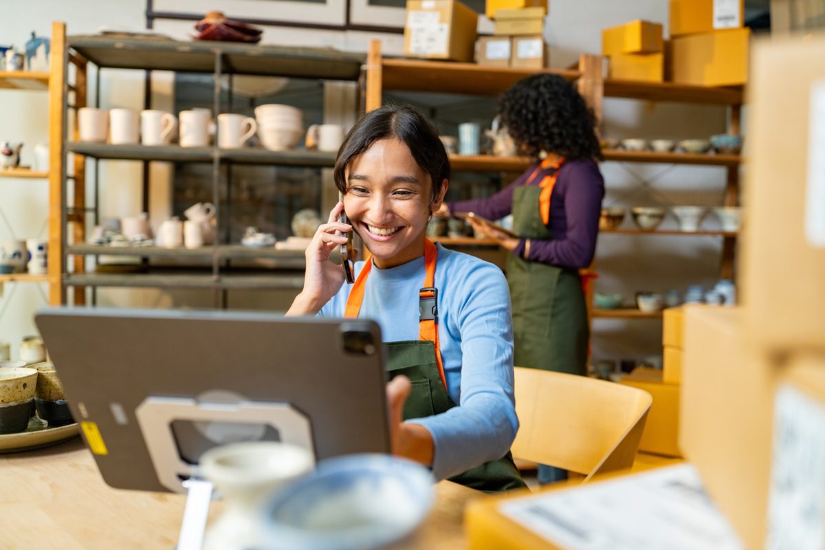 In a bustling ceramic shop, a young woman efficiently manages inventory and takes orders by phone, showcasing the seamless blend of traditional craftsmanship and modern business practices