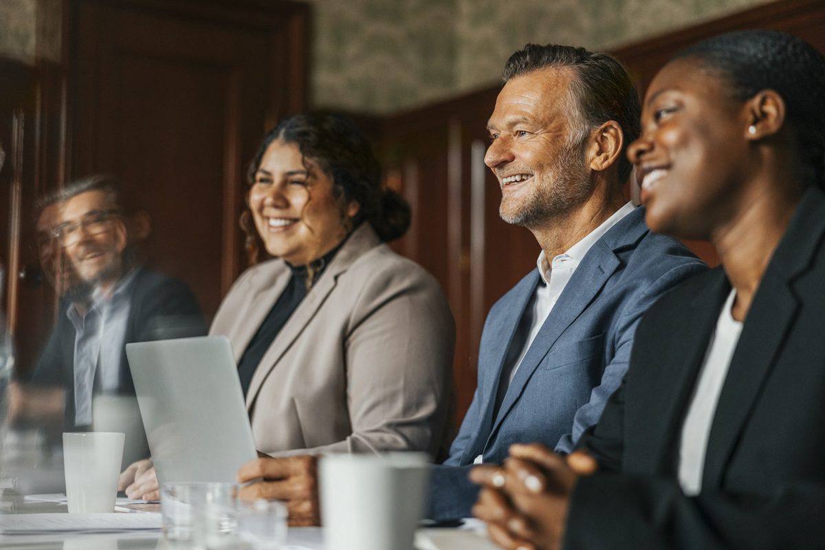 Team of smiling business professionals sitting next to each other during meeting in office board room