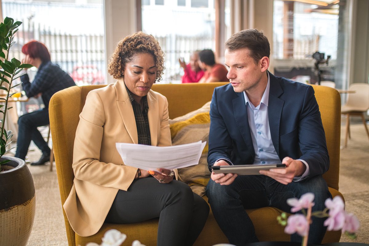 Diverse business colleagues having an informal business meting in a cafeteria. Sitting at a table having a discussion. Caucasian businessman is using digital tablet.