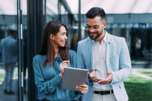 Shot of two confident colleagues walking and talking next to an office building. Businessman and businesswoman in meeting using digital tablet and discussing business strategy. Creative business persons discussing new project and sharing ideas while walking in front of their office building.