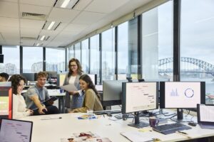 Multi racial colleagues planning strategies in team meeting at office. Male entrepreneur is pointing at reports. Computers are kept on desk.