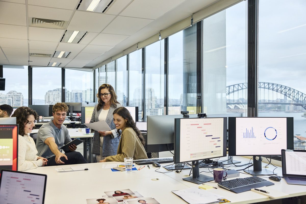 Multi racial colleagues planning strategies in team meeting at office. Male entrepreneur is pointing at reports. Computers are kept on desk.
