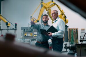 Robotics, people and engineer tablet with industrial collaboration and planning in warehouse. Factory, engineering and futuristic work of manufacturing management with discussion for cnc automation