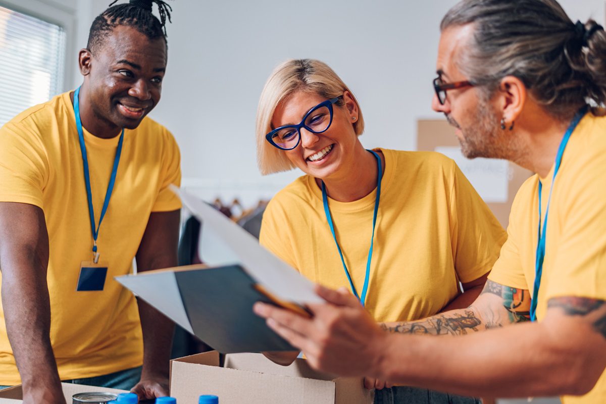 Multiracial volunteers working in community charity donation center. Volunteers putting clothes and other supplies in donation boxes while social worker is making notes. Focus on a blonde woman.