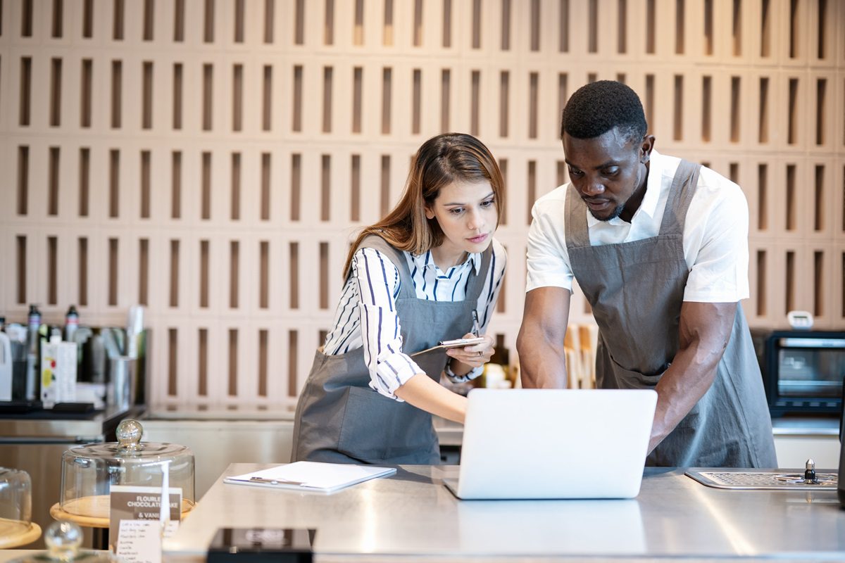 Offering Unique and Quality Products in Your Cafe. Diversity of Coffee Shop Ownerships having a discussion on marketing plan and strategy data on a laptop computer to increase customers at their cafe.