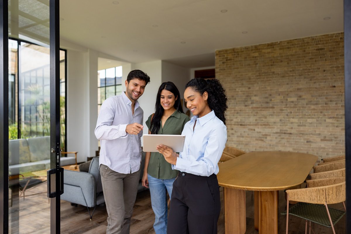 Real estate agent showing details of a house for sale to a couple on a digital tablet