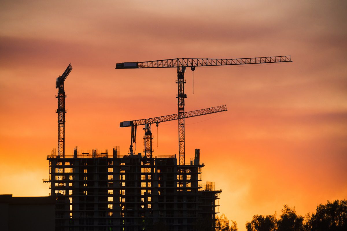This is a royalty free stock photograph of a back lit building with industrial construction cranes at sunset in Miami, Florida Photographed with a Nikon D800 DSLR camera. Creative Content Brief 686998297