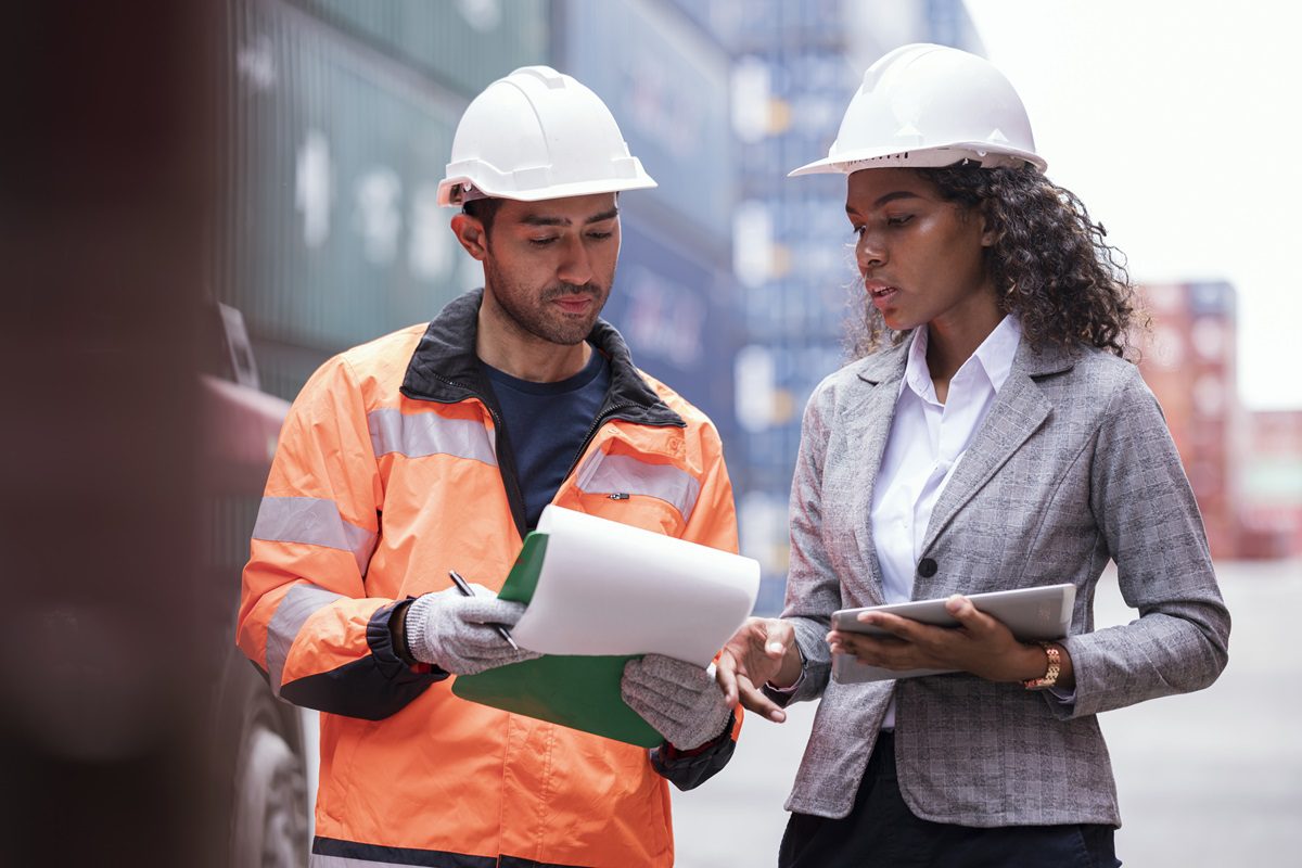 Shipping Container Tracking and Tracing. An African American shipper and Asian male loading controller is checking and tracking shipment status on report during container loading and unloading operation in a logistics center.