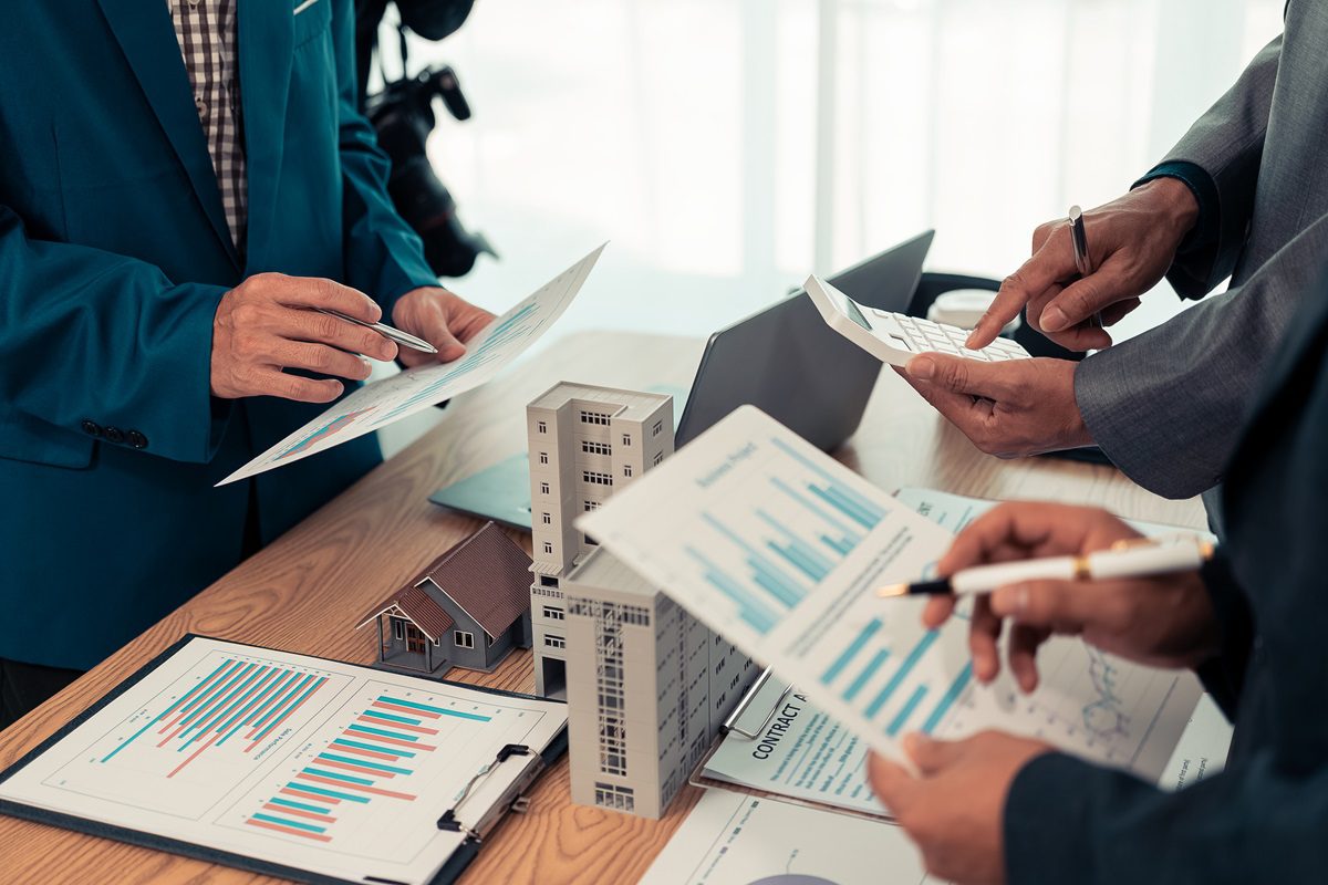 Real estate entrepreneurs meeting to sell a house, discussing real estate deals, with house plans on the table, symbolizing real estate investment and negotiations.