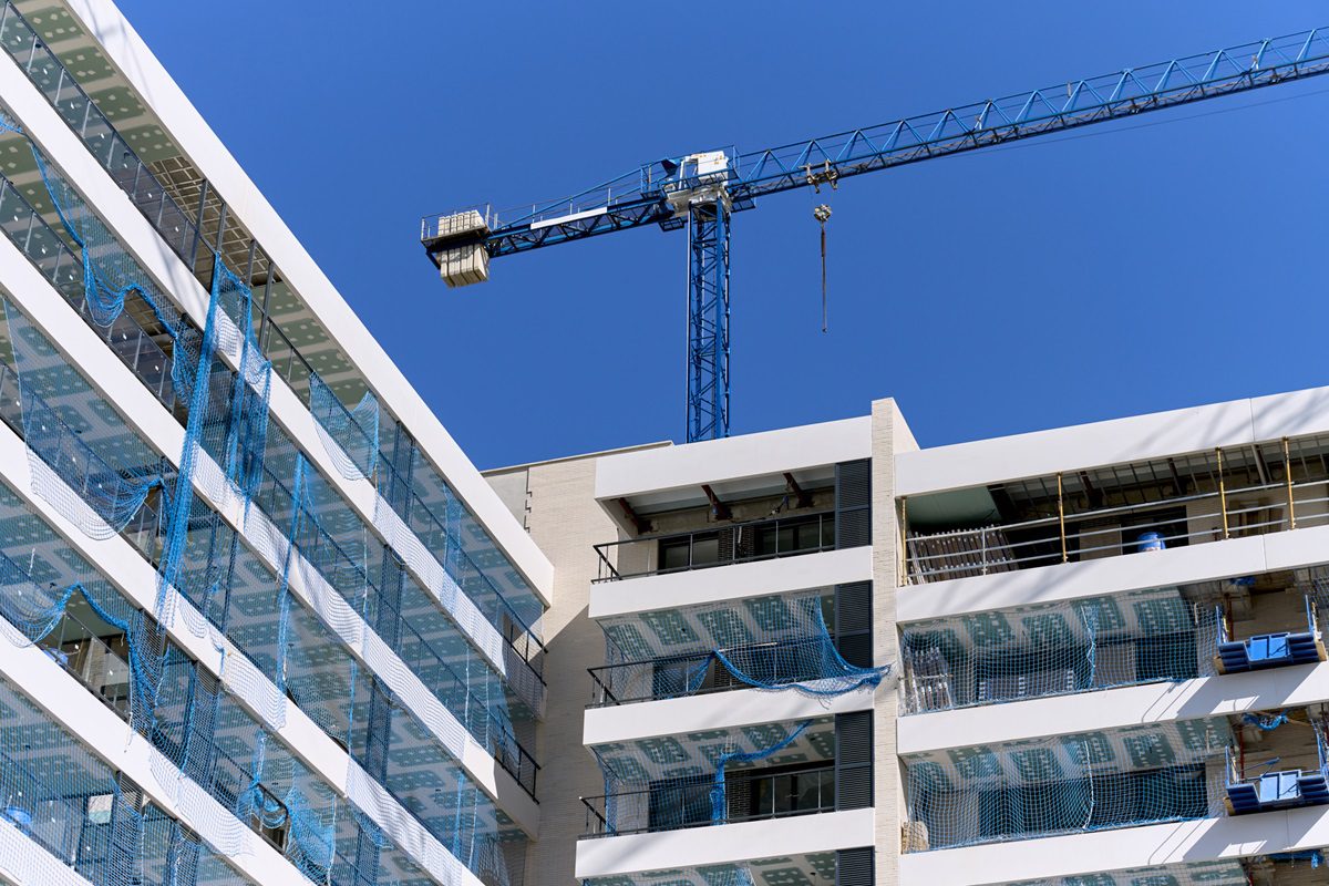 low angle view of a building under construction with a metal crane on the roof and a blue sky in the background.