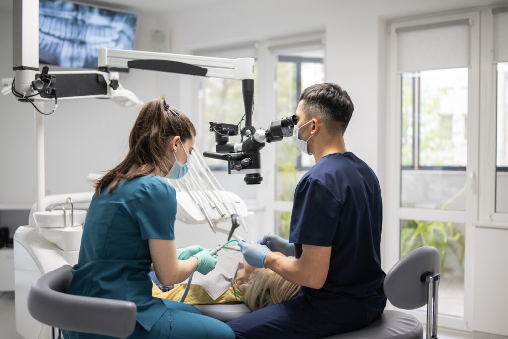 A dentist carefully examines a patient&rsquo;s teeth using a dental microscope in a modern clinic.