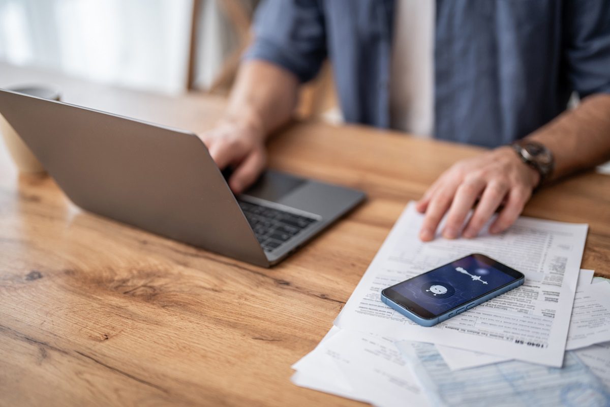 Adult man working from home using ai voice assistant on phone and laptop