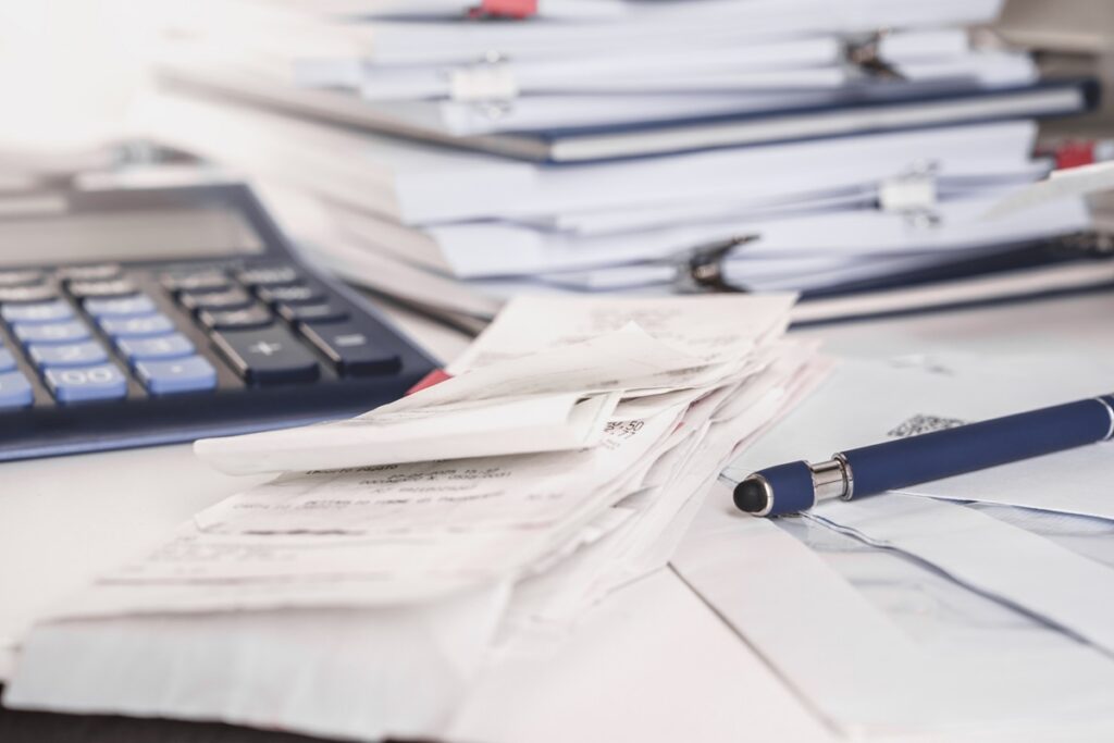 Stack of receipts with calculator. Lots of documents, papers and notepads on a desk.